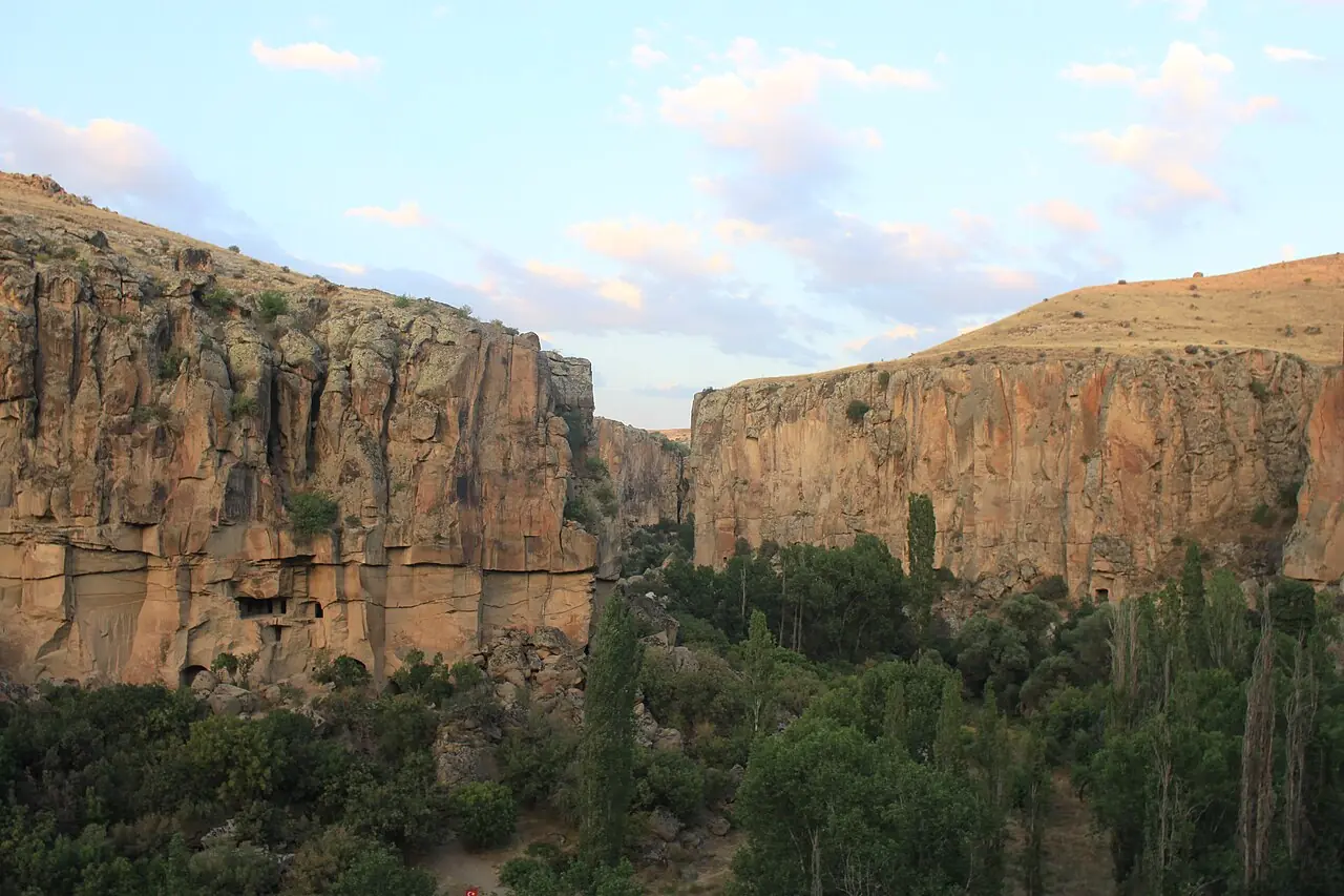 Tall Ihlara Valley cliffs frame dense green trees beneath a blue sky.