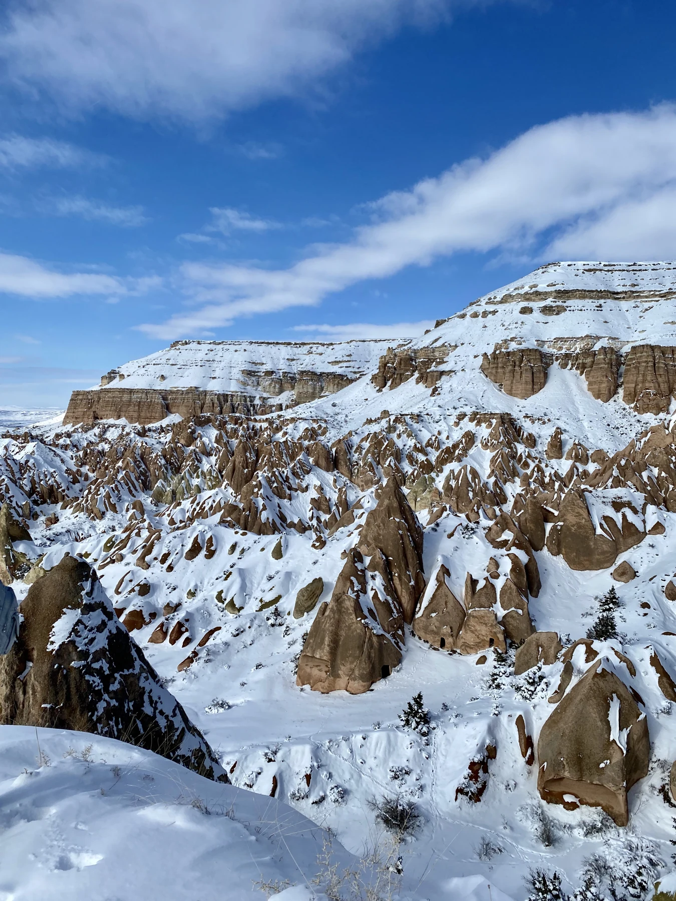 Snow blankets the fairy chimneys and rocky slopes of Göreme beneath a blue winter sky.